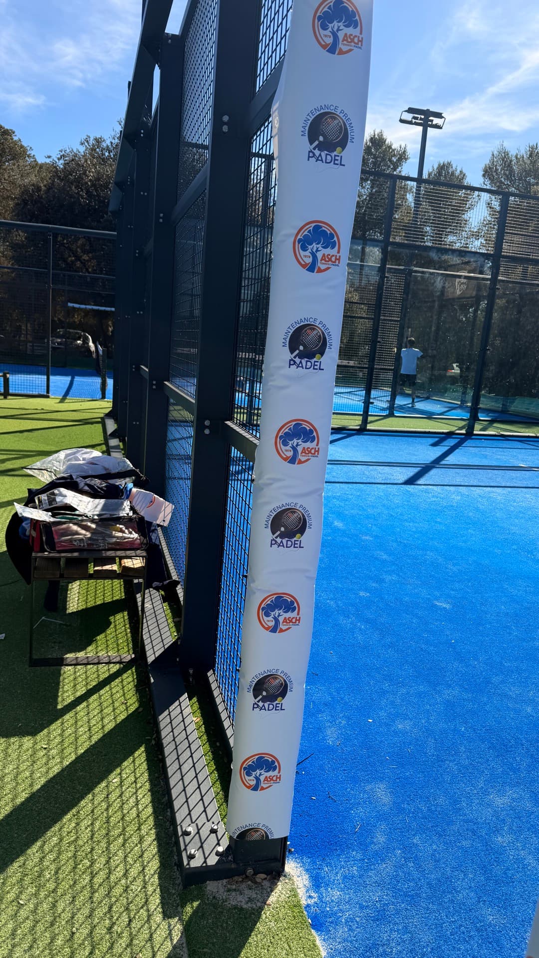 Protections de poteaux blanches floquées du logo Padel Maintenance Premium sur un court bleu